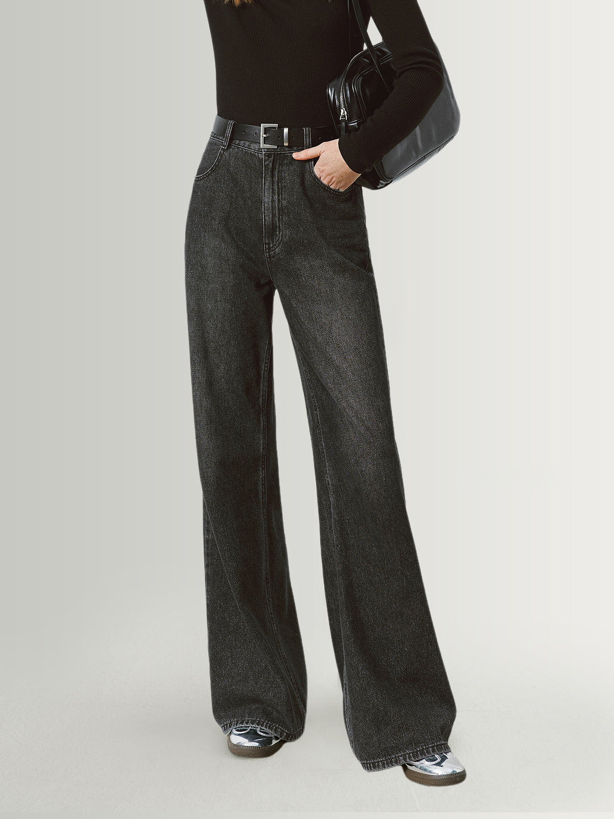 Person wearing black high-waisted jeans on a light gray background