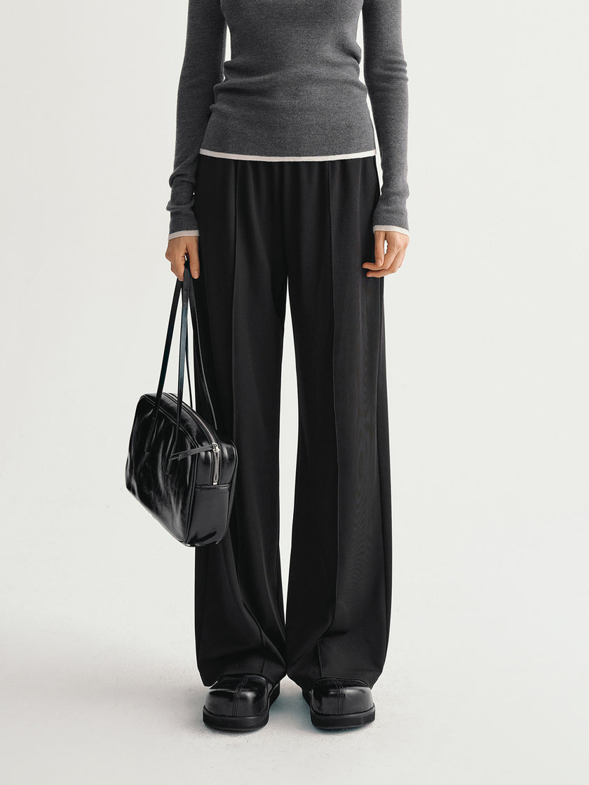 Person wearing a gray top and black wide-leg pants holding a black handbag on a light gray background