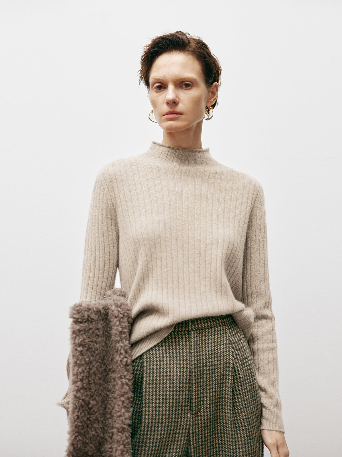 Woman wearing a beige sweater and plaid skirt against a plain background