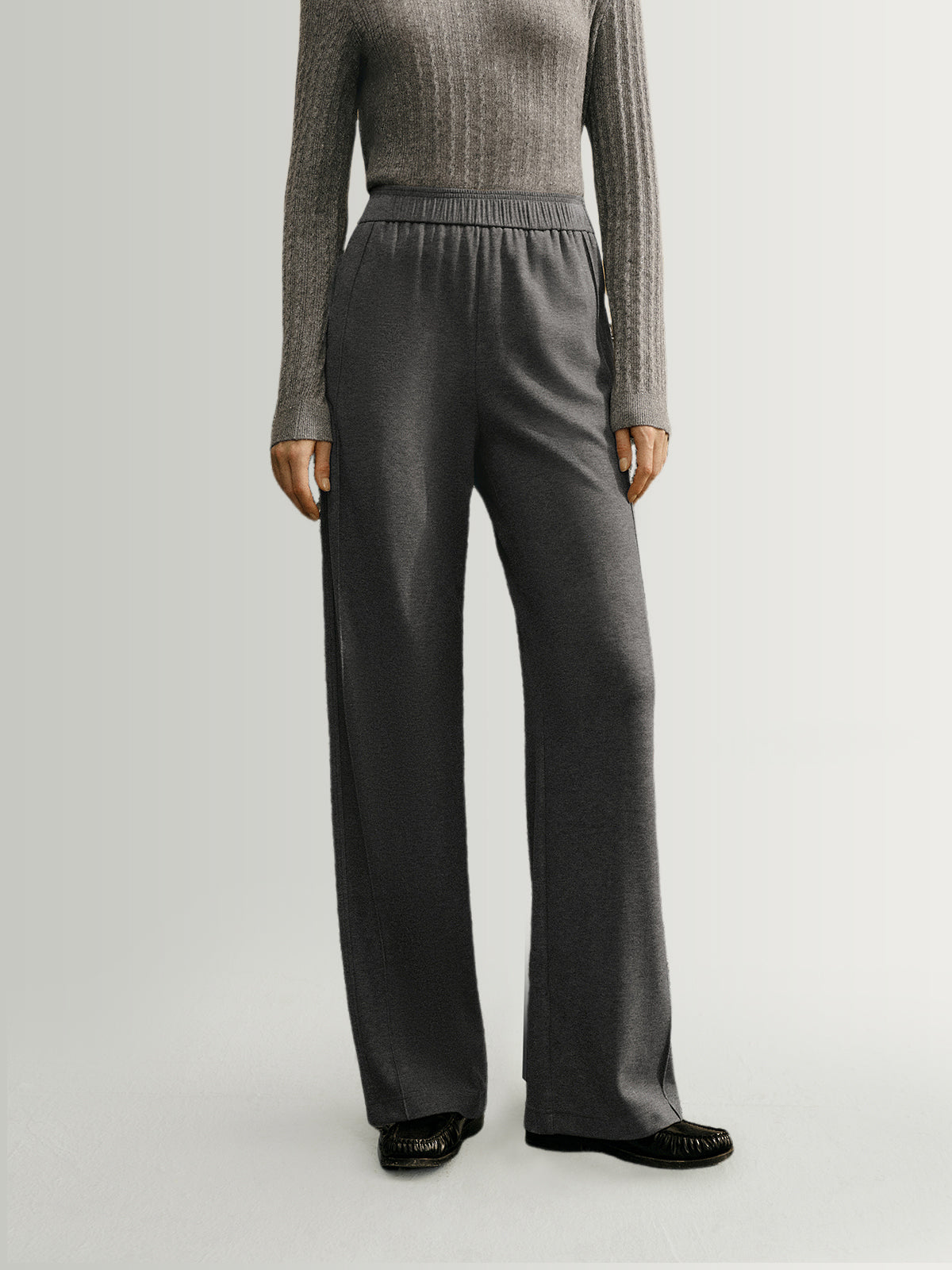 Person wearing a gray sweater and dark gray wide-leg pants on a light gray background