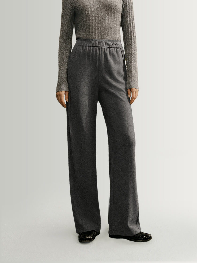 Person wearing a gray sweater and dark gray wide-leg pants on a light gray background