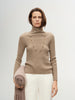 Woman wearing a beige turtleneck sweater holding a folded blanket against a plain background