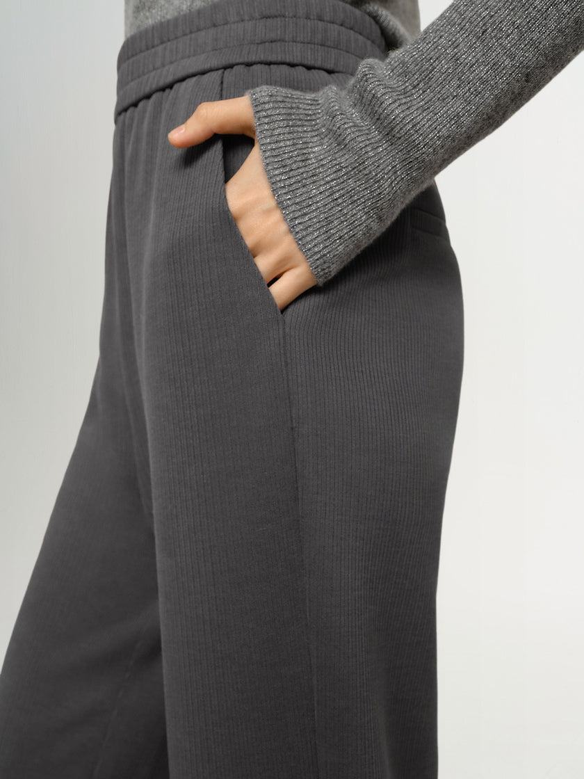 Person wearing gray ribbed knit pants and sweater on a light gray background