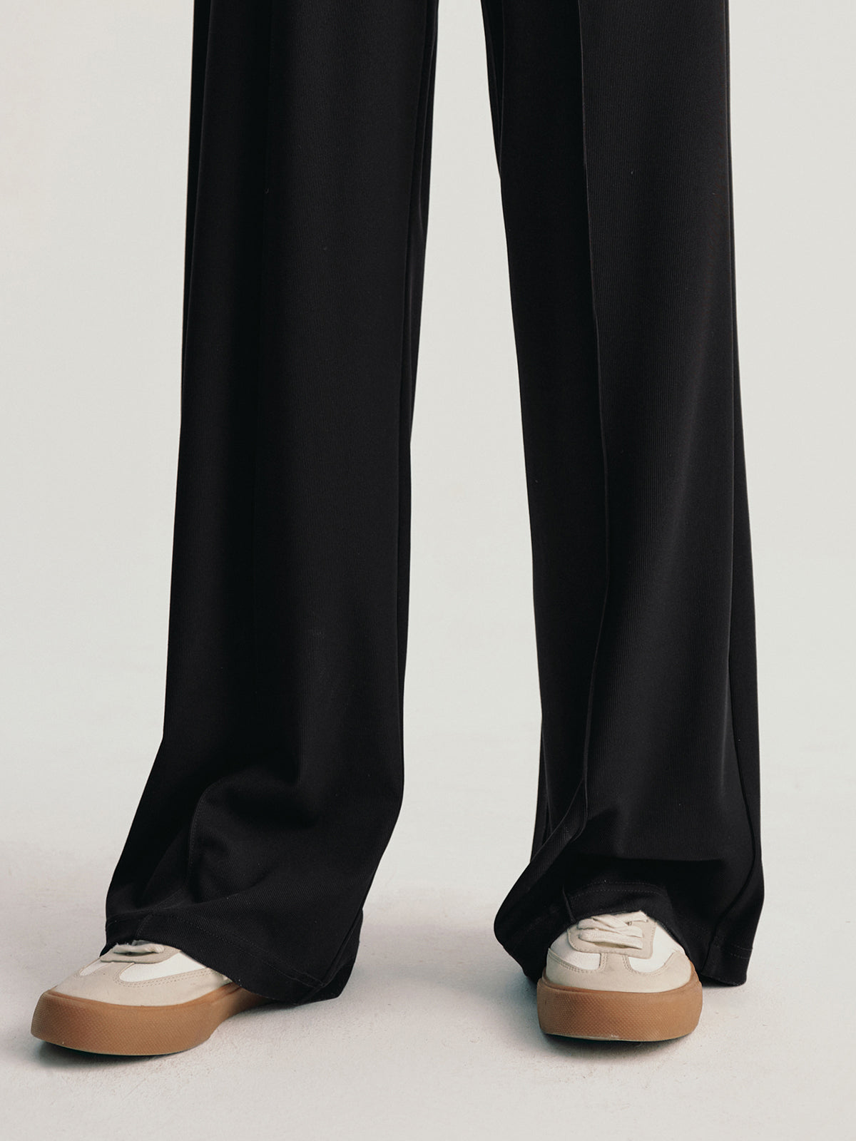 Black wide-leg pants worn with white sneakers on a light gray background