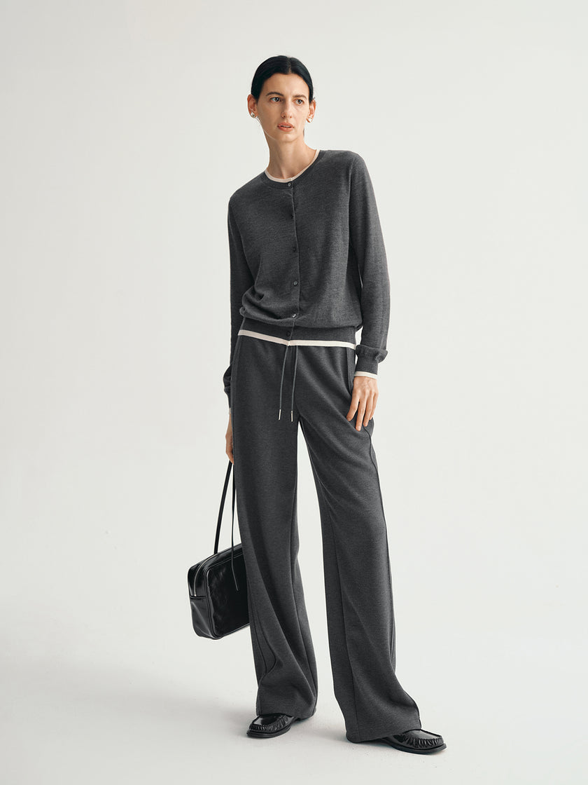 Person wearing a dark gray outfit with wide-leg pants and a black bag on a light gray background