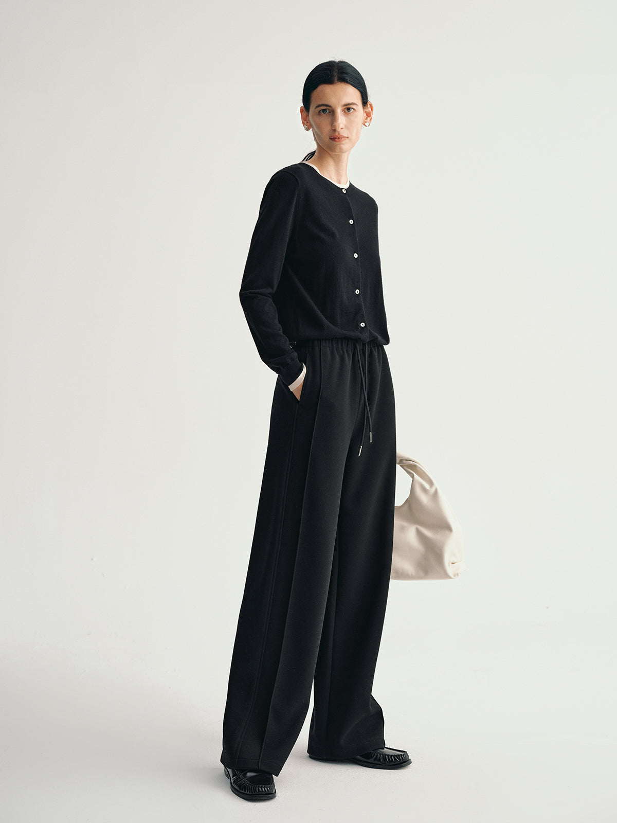 Person wearing a black outfit with wide-leg pants on a light gray background