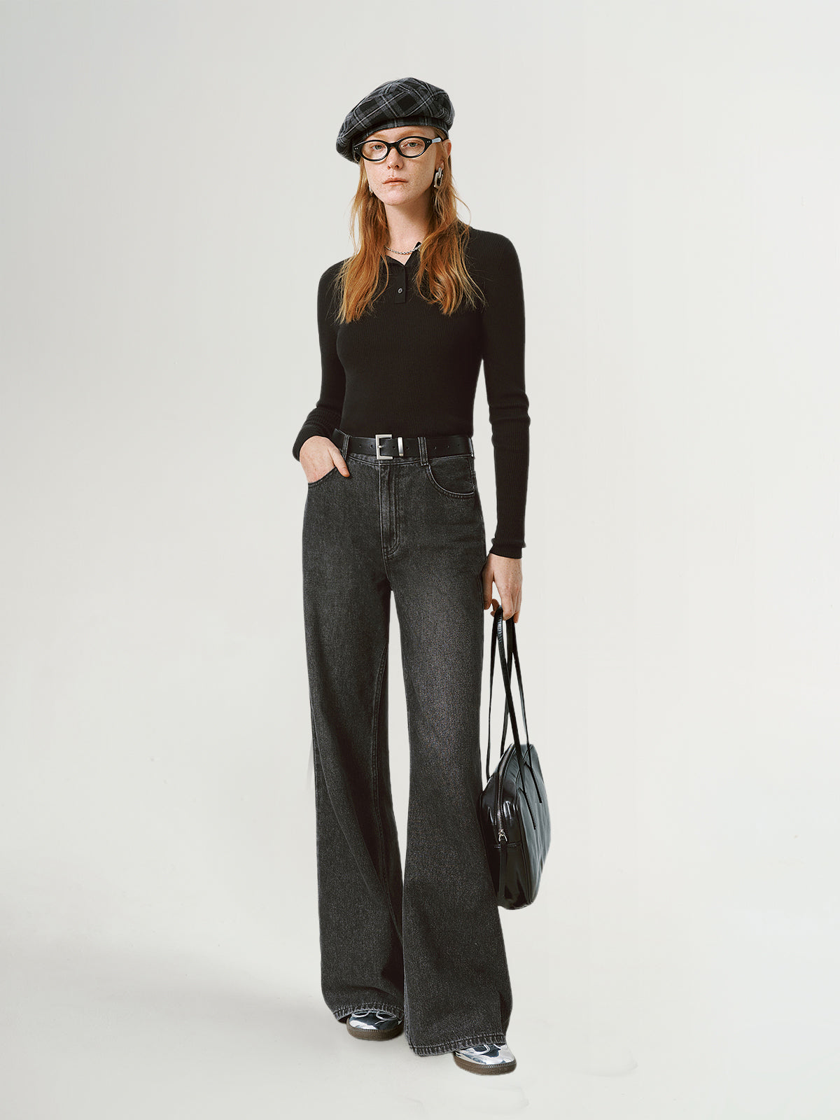 Person wearing a black outfit with a beret and holding a bag on a white background