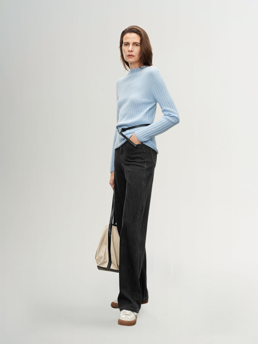 Woman wearing a light blue sweater and black pants against a plain background