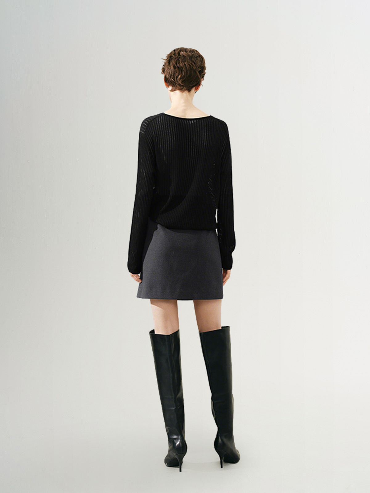 Model wearing a rib knit sweater with a relaxed fit, paired with a short skirt and knee-high boots.