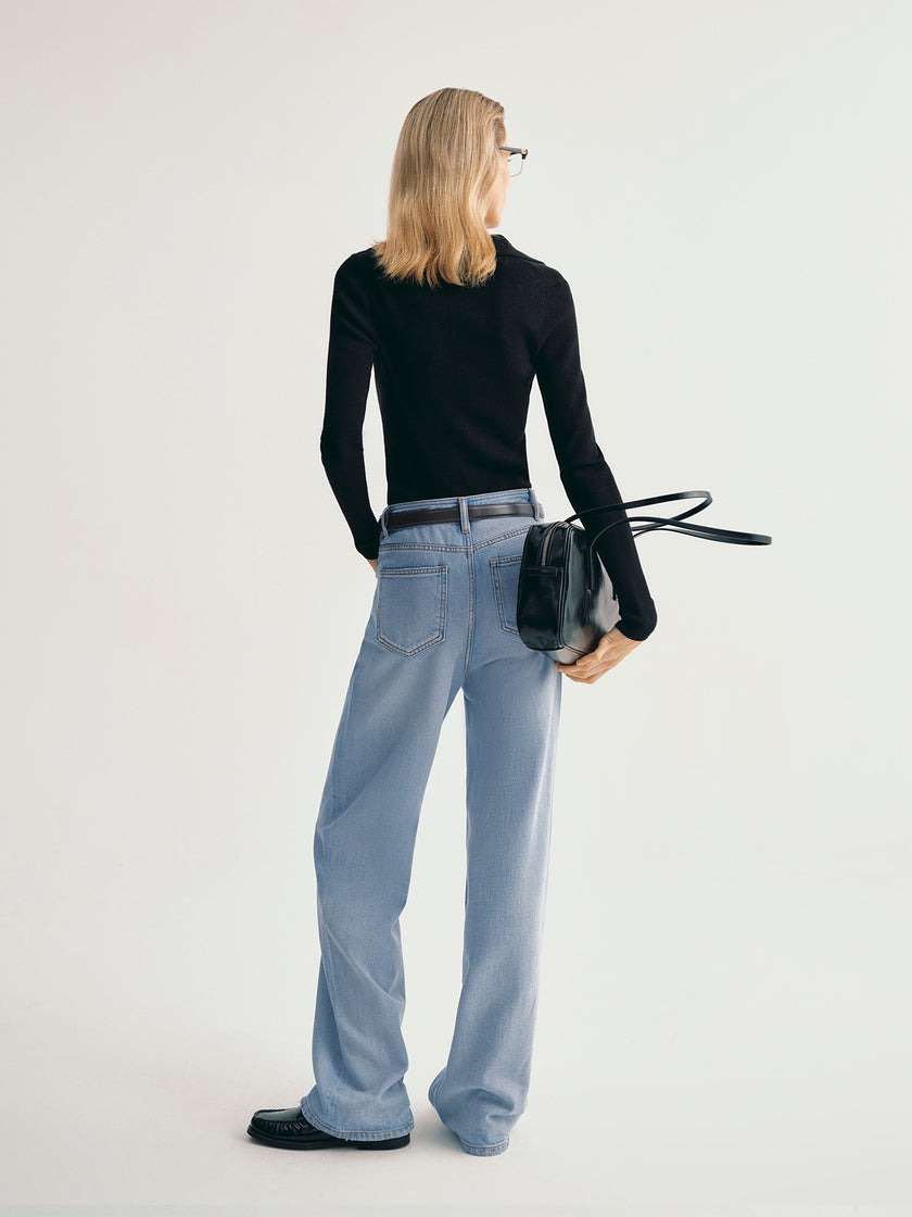 Person wearing light blue jeans and a black top, standing against a plain background
