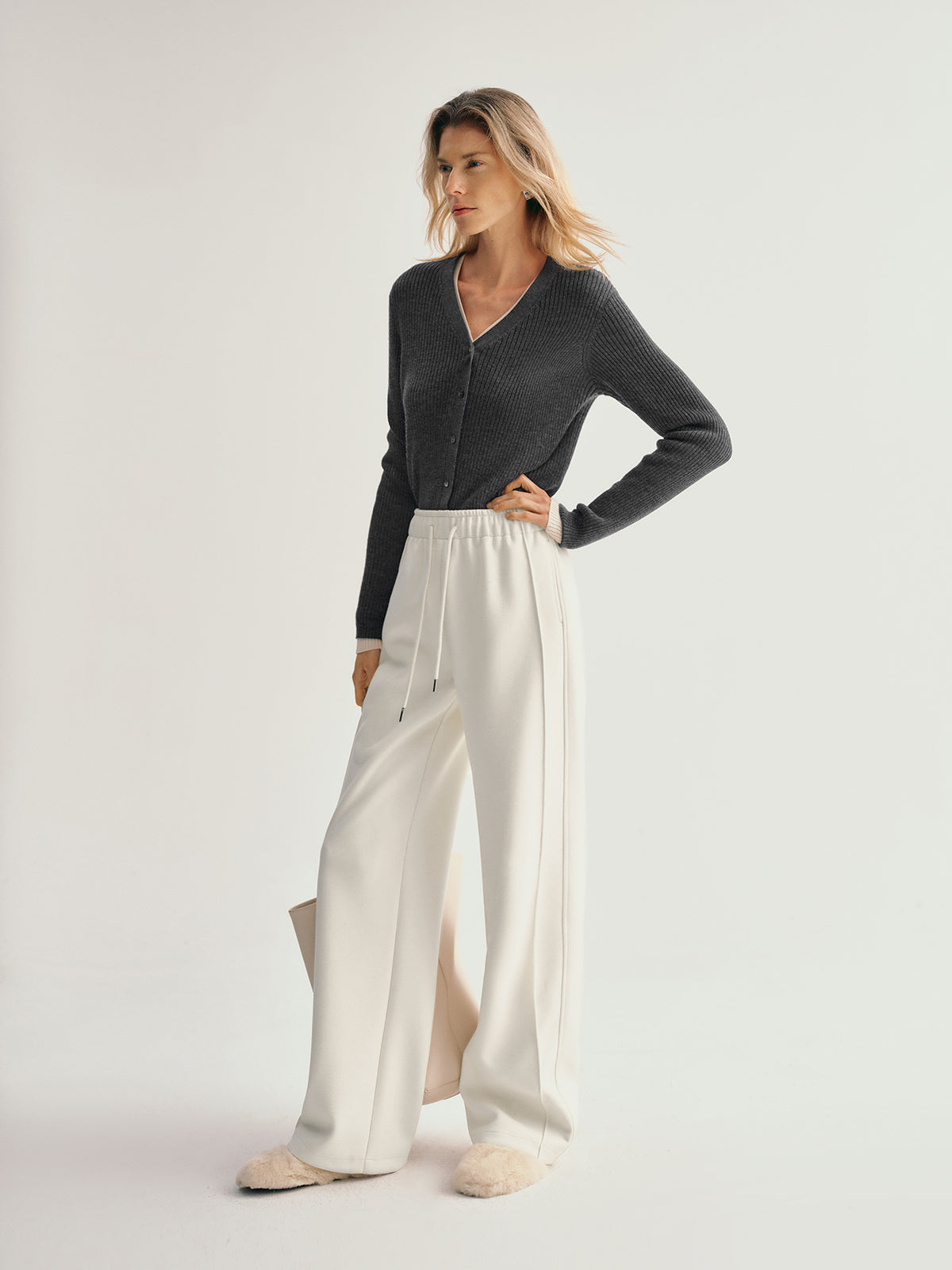 Woman wearing a dark gray cardigan and white pants on a light gray background