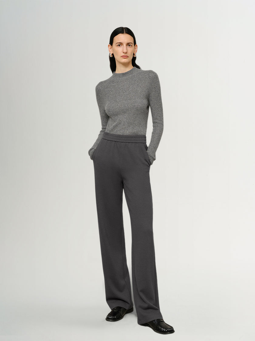 Person wearing a gray sweater and pants on a white background