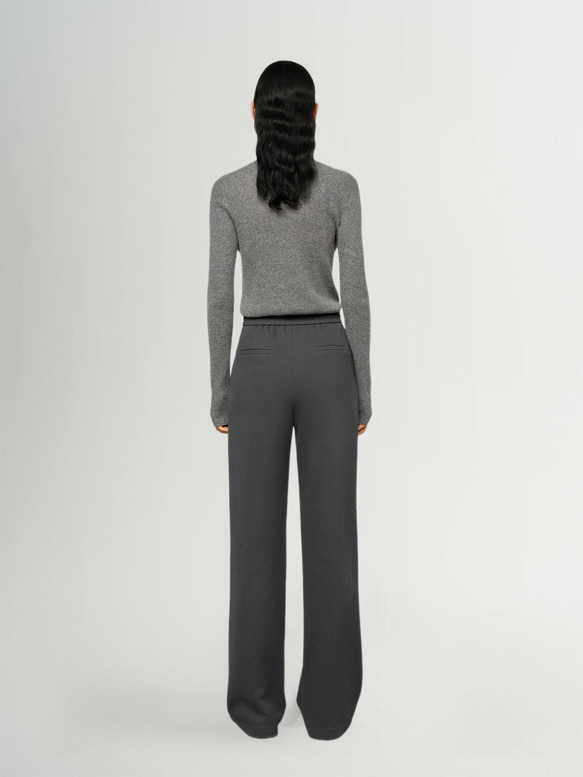 Person wearing a gray sweater and dark gray pants on a white background