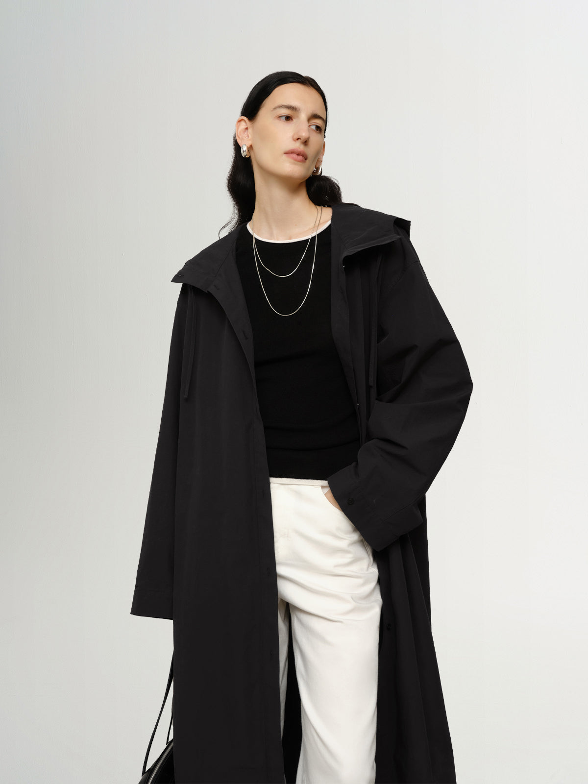 Person wearing a black coat over a black top and white pants on a plain background