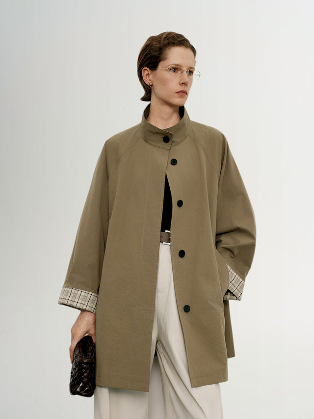 Model wearing a long olive green coat with a plaid lining on a white background
