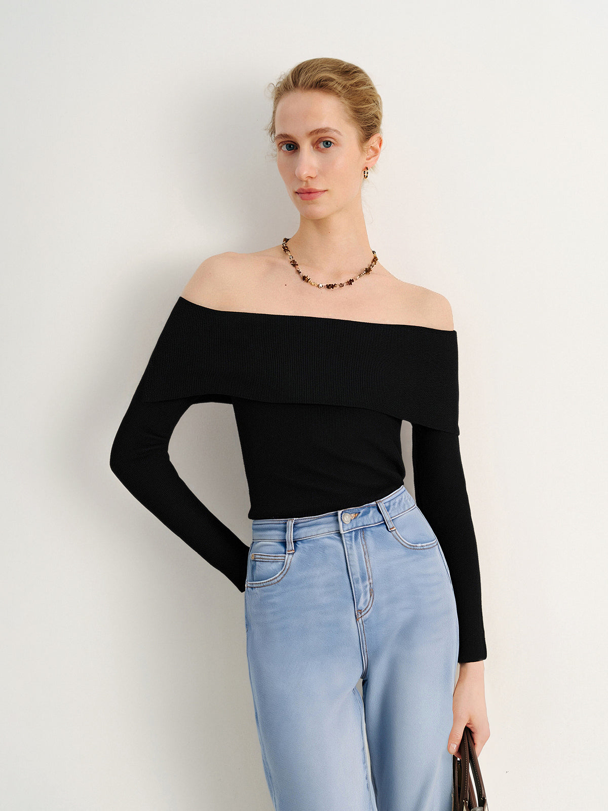 Woman wearing a black off-shoulder top and light blue jeans against a white background