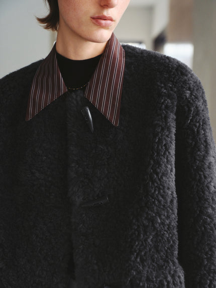 Person wearing a dark textured coat with a striped collar indoors