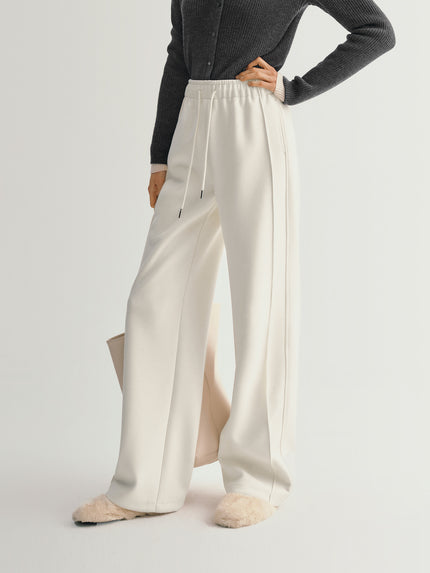 Person wearing white wide-leg pants with a gray top on a light gray background