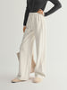 Person wearing white wide-leg pants with a gray top on a light gray background
