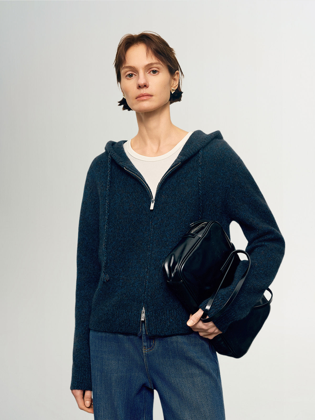 Woman wearing a dark blue hoodie holding a black bag against a light gray background