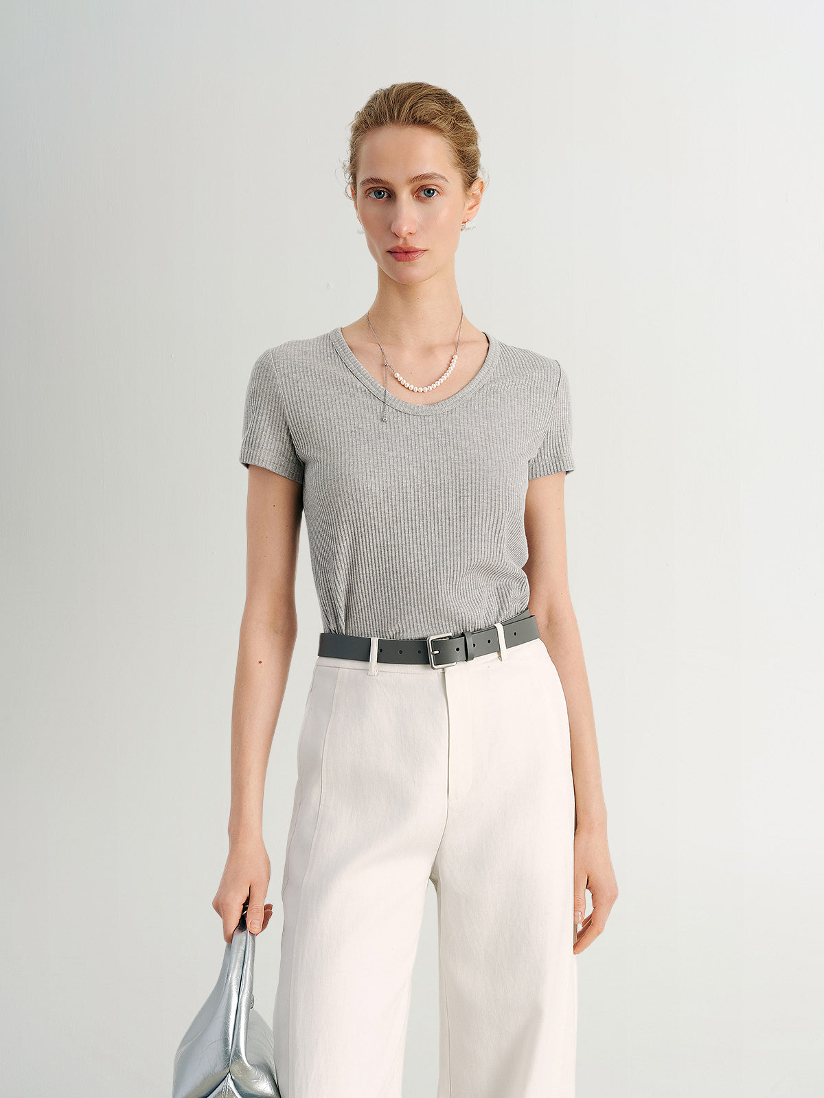 Woman wearing a gray checkered top and white pants against a light gray background