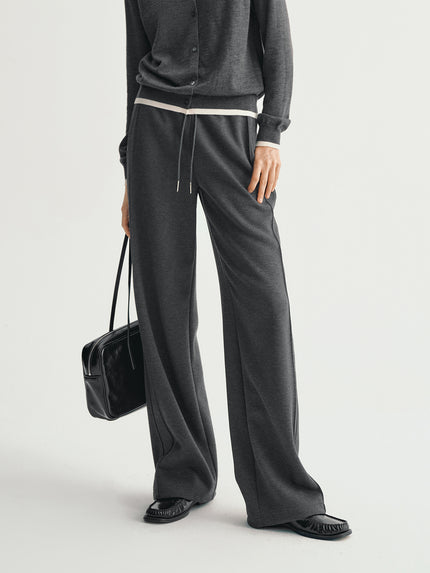 Person wearing a gray outfit with wide-leg pants and holding a black handbag on a light gray background