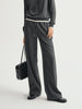 Person wearing a gray outfit with wide-leg pants and holding a black handbag on a light gray background