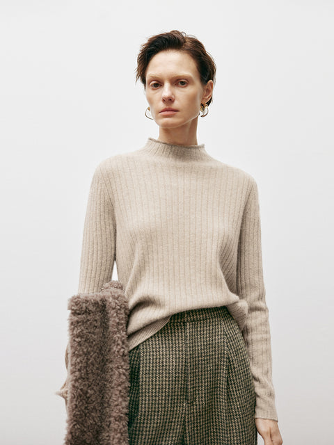 Woman wearing a beige sweater and plaid skirt against a plain background