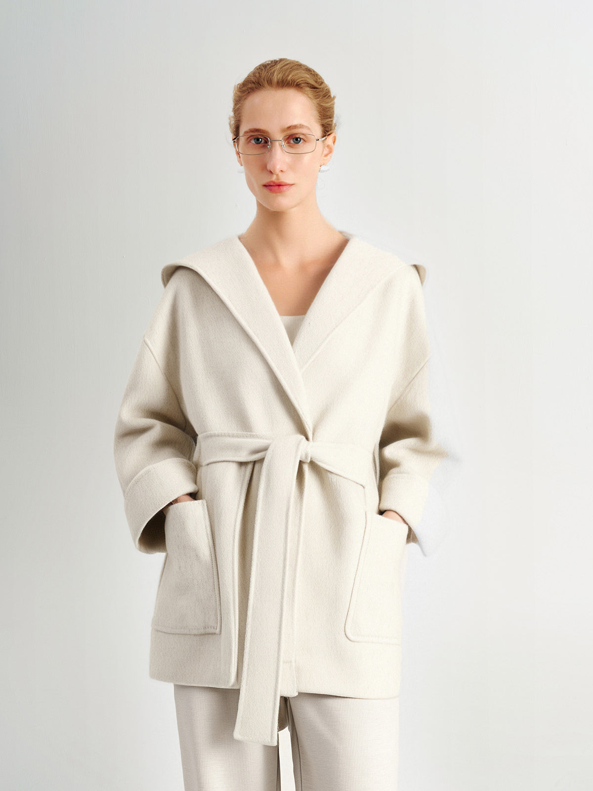 Woman wearing a light beige coat and pants on a plain background