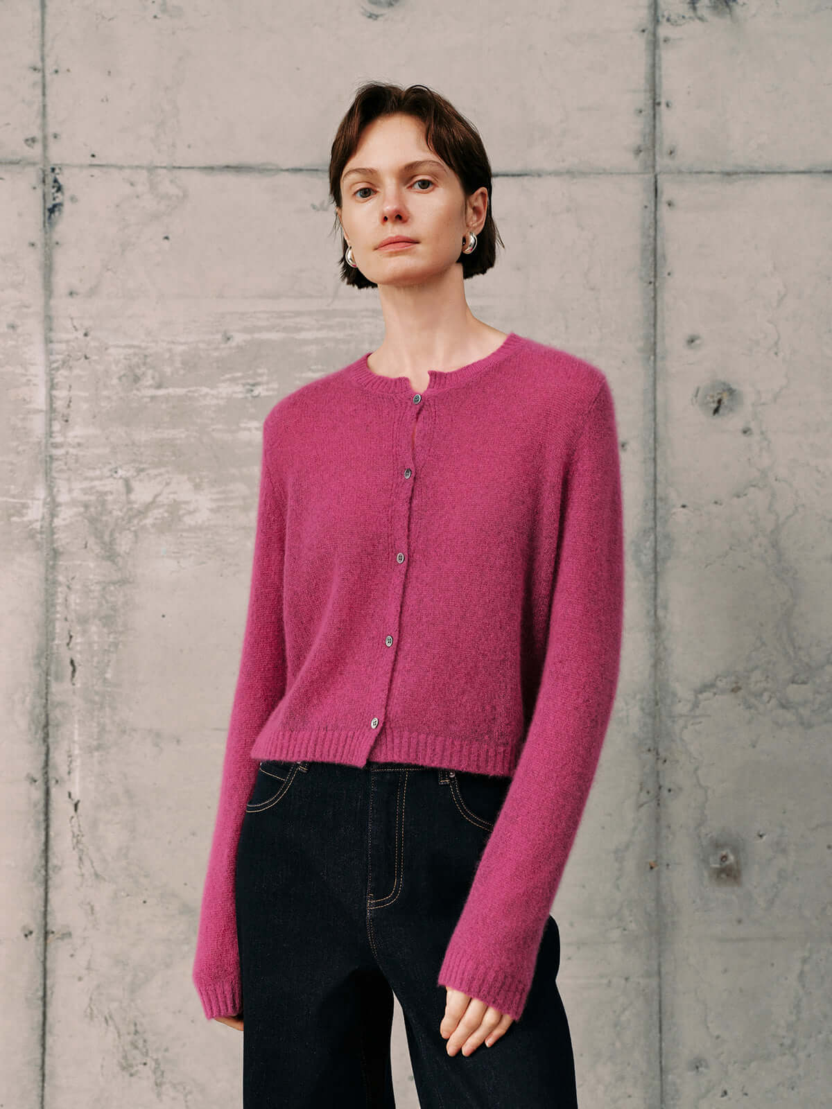 Silk-Cashmere Cardigan in vibrant pink, styled with dark jeans against a textured backdrop.