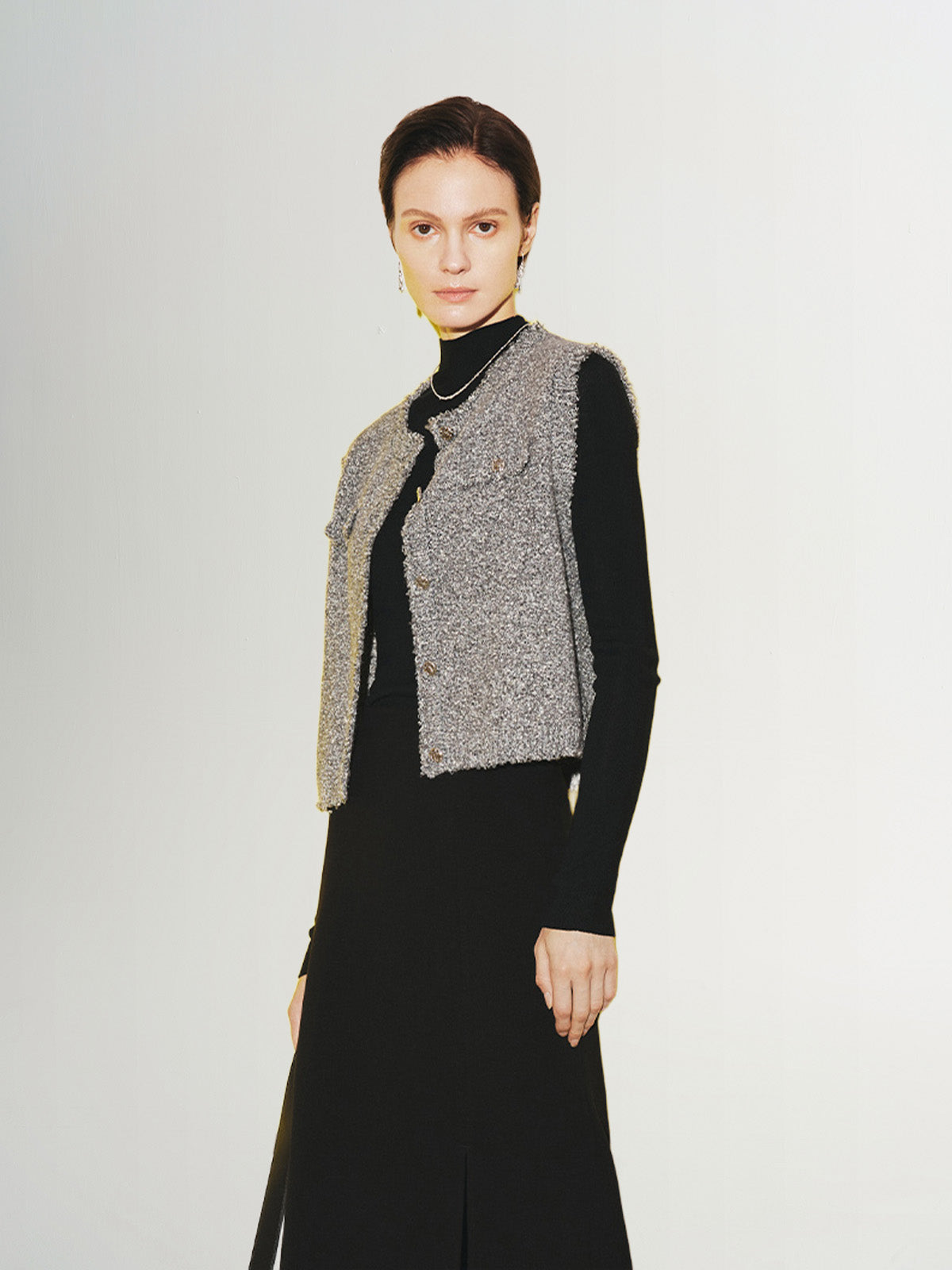 A woman wearing a gray tweed knit vest over a black top and a long black skirt.