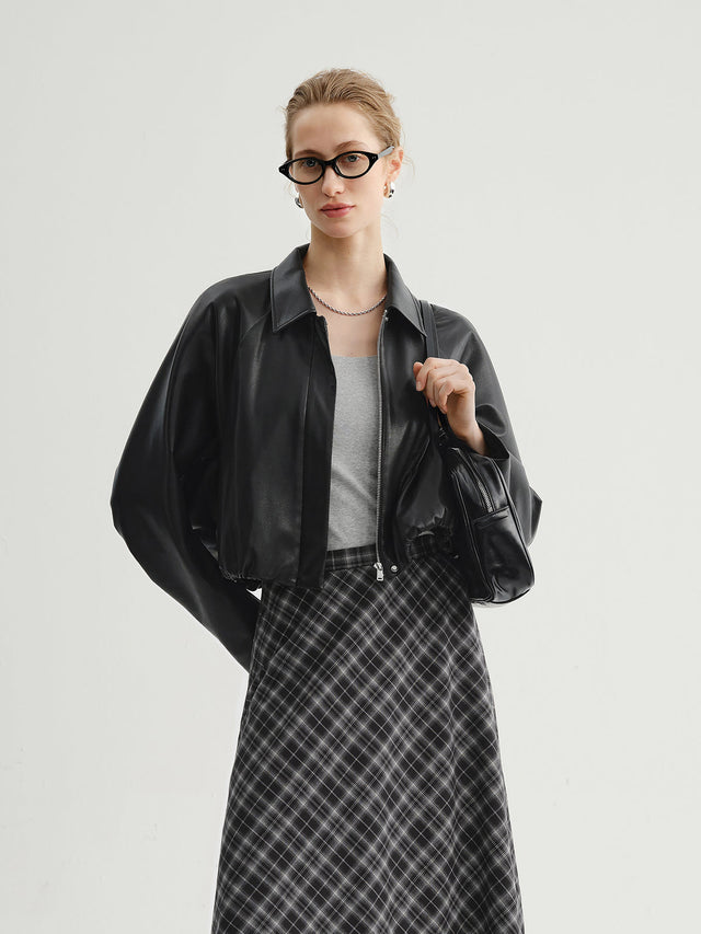 Model wearing a black leather jacket, gray top, and plaid skirt on a light background