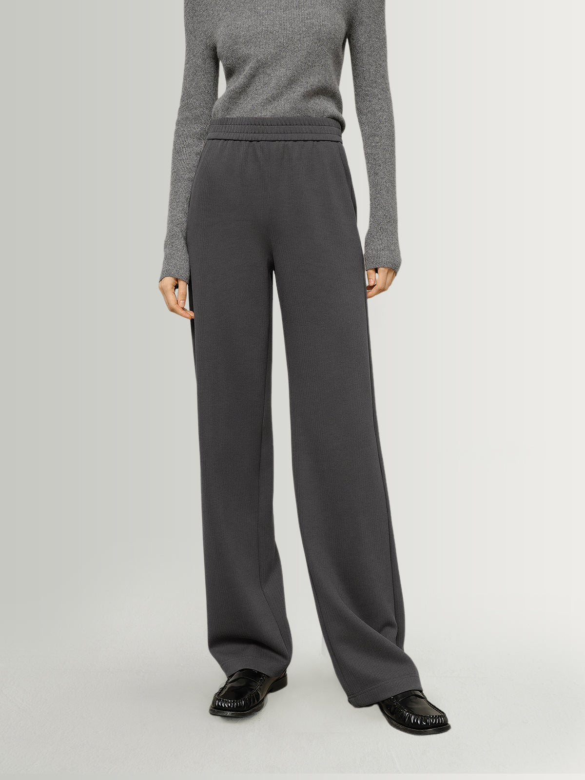 Person wearing gray sweater and dark gray pants on a light gray background