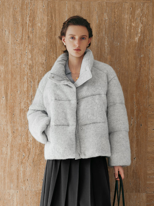 Load image 1 in gallery view. Person wearing a gray puffer jacket against a wooden background