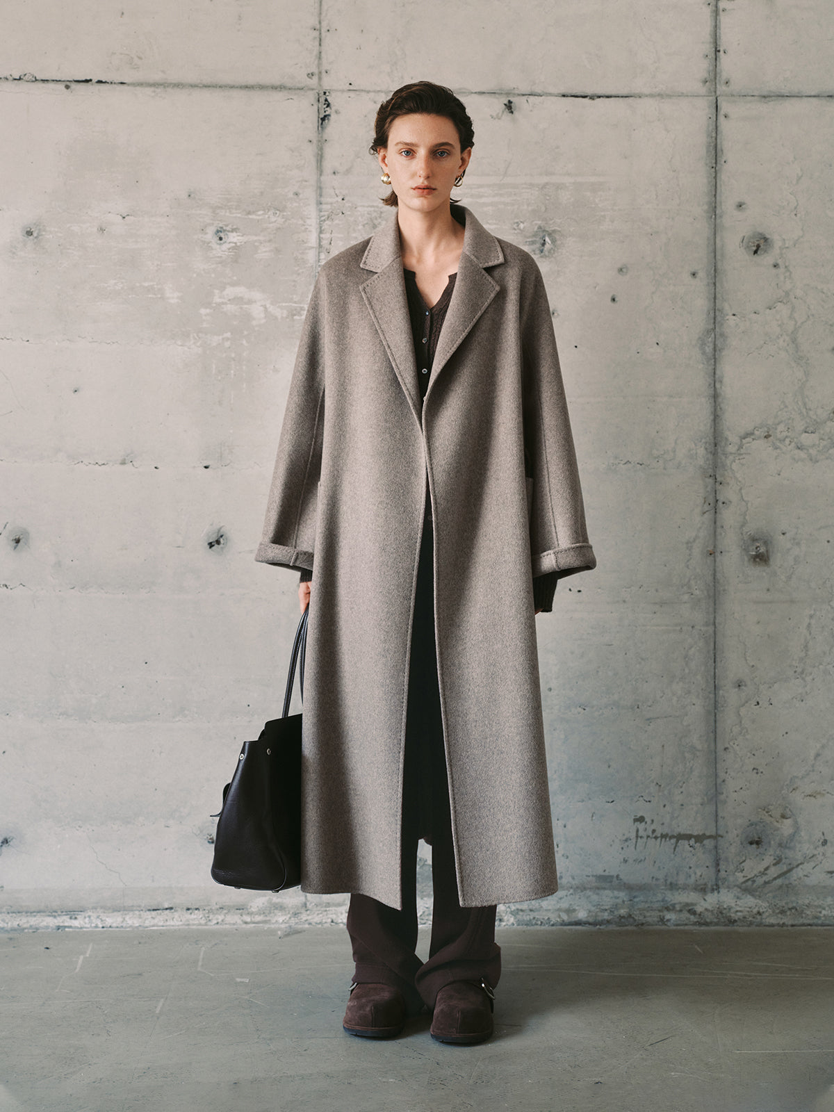 Person wearing a long warm gray coat against a concrete wall.