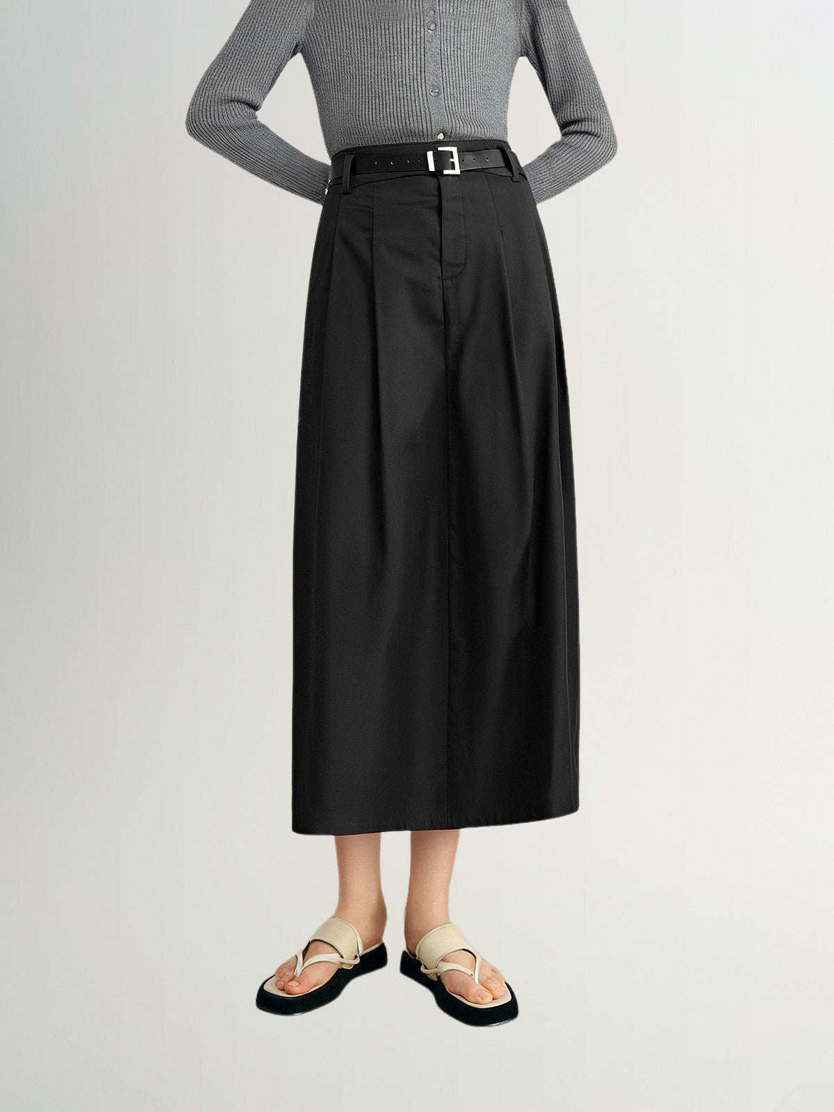 Person wearing a gray sweater and black skirt on a white background