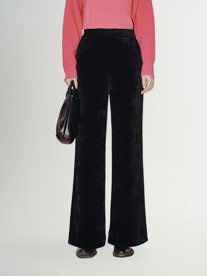 Woman wearing women's wide leg trousers , paired with a pink sweater and a black bag, showcasing a modern and elegant silhouette.