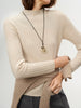Person wearing a beige sweater with a necklace on a light gray background