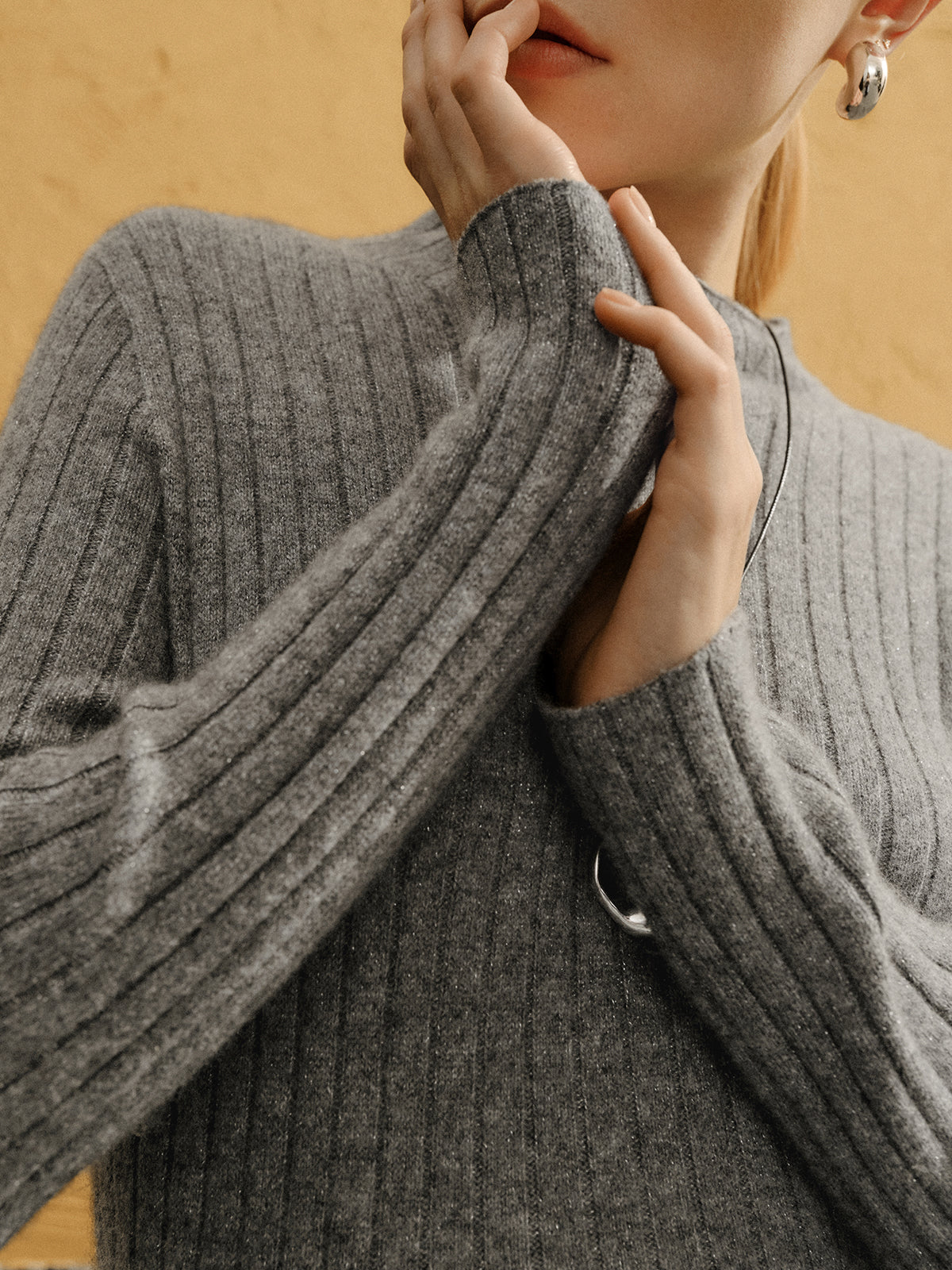 Person wearing a gray ribbed sweater with a neutral background