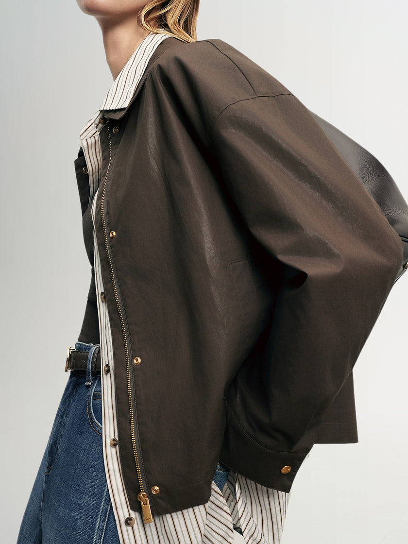 Person wearing a brown jacket with a white shirt and blue jeans on a gray background