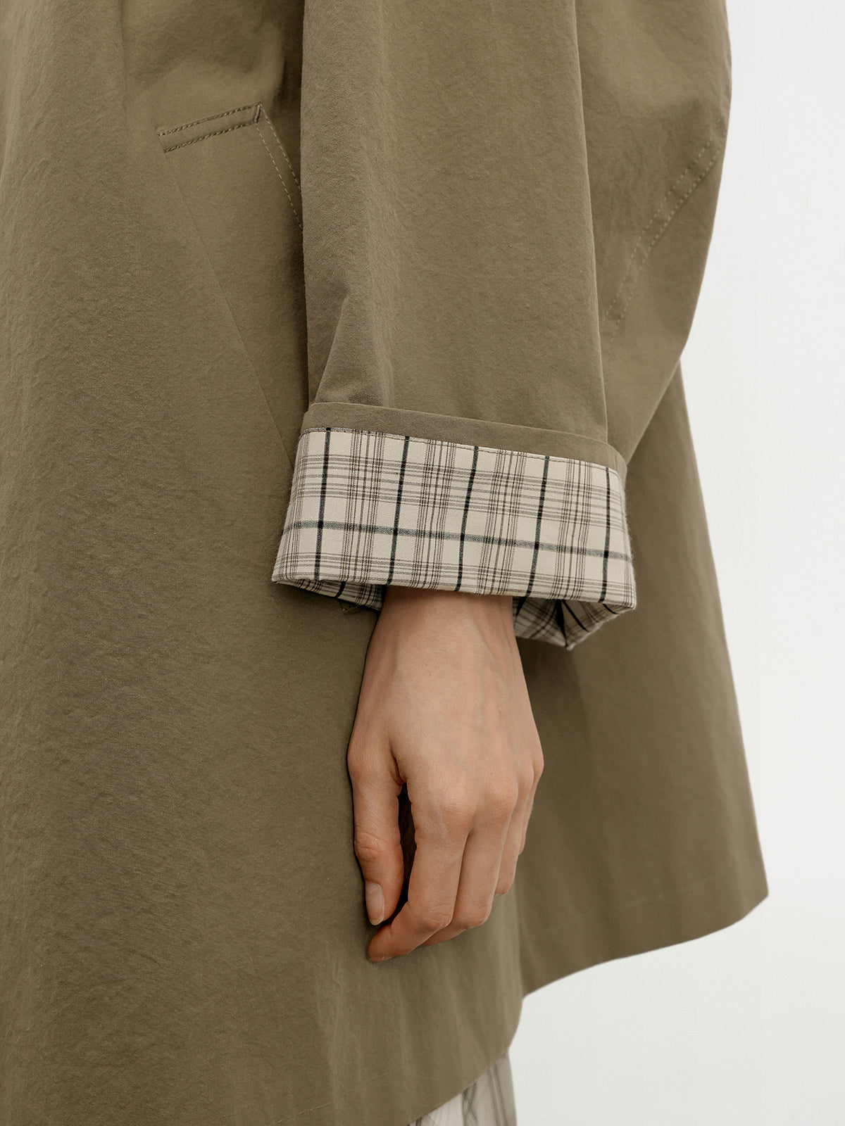 Close-up of model wearing a green coat with plaid cuffs on a white background