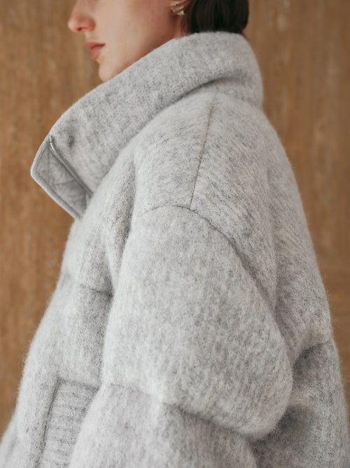 Load image 1 in gallery view. Person wearing a gray coat against a wooden background