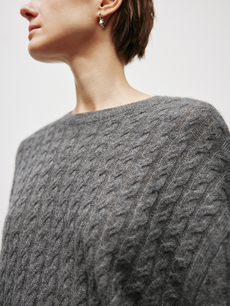 Close-up of a women wearing a gray cable knit sweater on a light background