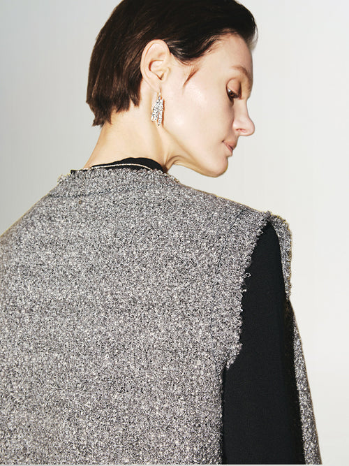 Load image 1 in gallery view. Close-up of a woman wearing a stylish Tweed Knit Vest with textured gray fabric and elegant earrings.