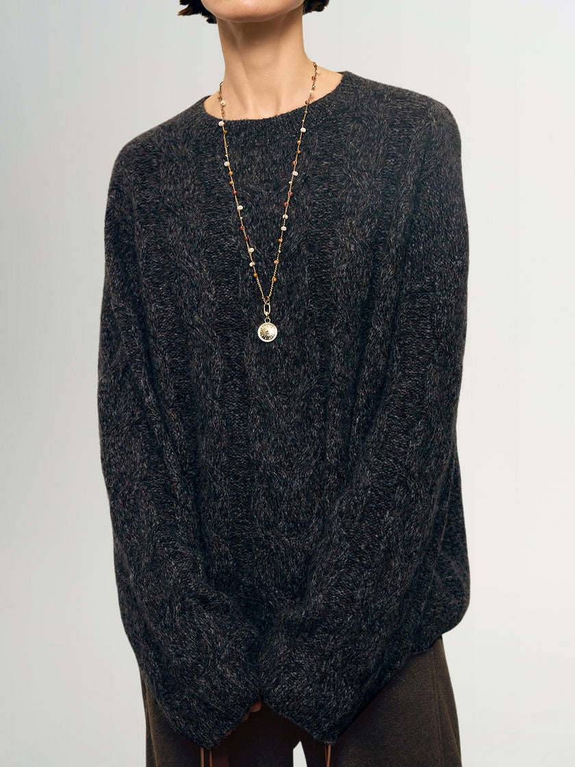 Person wearing a dark gray sweater and a long necklace with a pendant on a light gray background