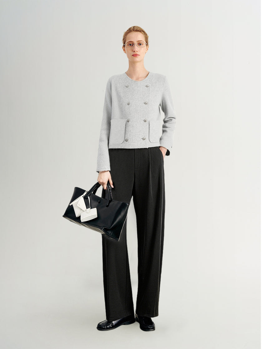 Person wearing a light gray sweater and black pants, holding a black handbag with a white bow on a white background