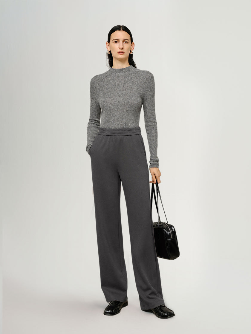 Person wearing a gray sweater and pants holding a black bag on a white background