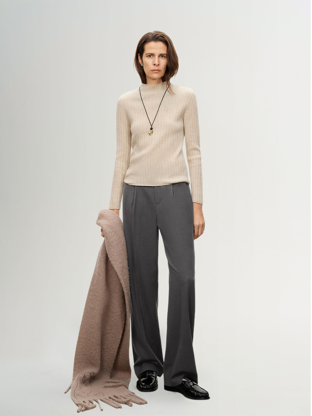 Woman wearing a beige sweater and gray pants with a brown scarf on a white background