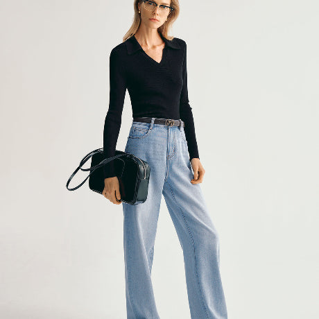 Woman wearing a black top and light blue jeans holding a black handbag on a white background