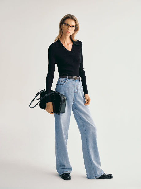 Woman wearing a black top and light blue jeans holding a black handbag on a white background